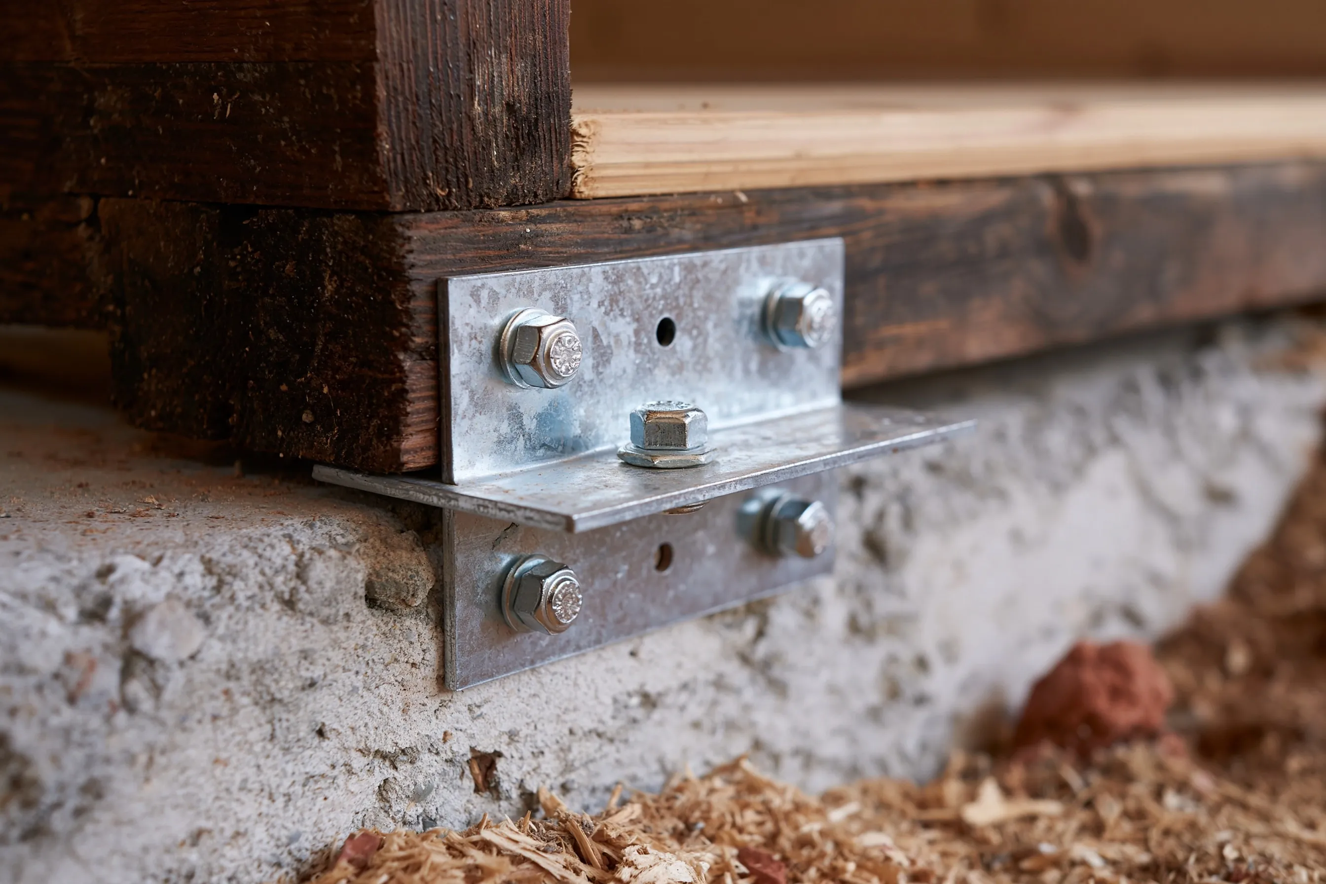 A galvanized steel connector plate fastening floor framing to a concrete stem wall in a crawlspace